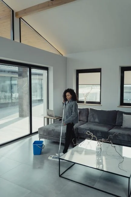 A woman carefully wraps a sofa in protective material while packing boxes in a bright room.